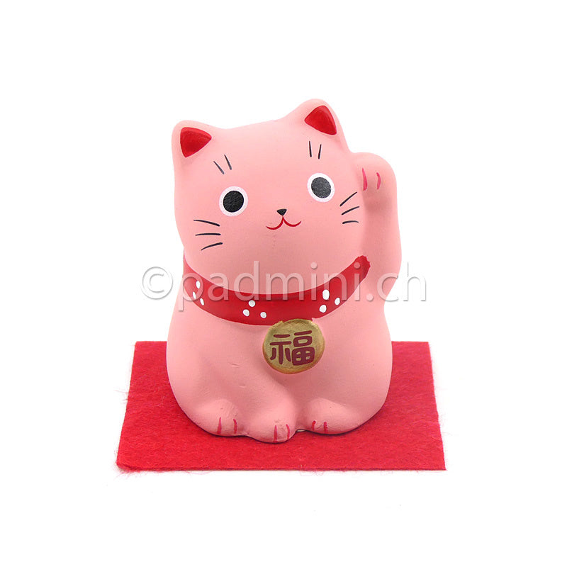 Japanische Maneki-Neko Glückskatze in Rosa mit roten Details, erhobener Pfote und Glückszeichen auf der Halsplakette.