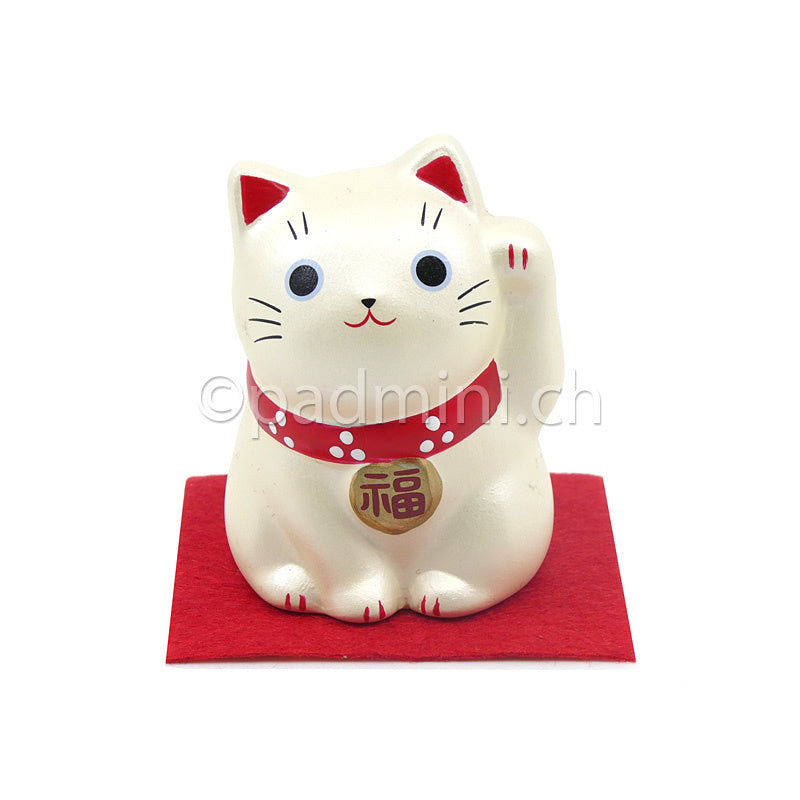 Japanische Maneki-Neko Glückskatze in Cremeweiss mit roten Details, erhobener Pfote und Glückszeichen auf der Halsplakette.