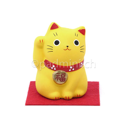 Japanische Maneki-Neko Glückskatze in Gelb mit roten Details, erhobener Pfote und Glückszeichen auf der Halsplakette.