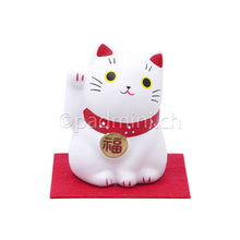Japanische Maneki-Neko Glückskatze in Weiss mit roten Details, erhobener Pfote und Glückszeichen auf der Halsplakette.